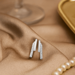 Nipura 925 Sterling Silver CZ Huggie Hoop Earrings on satin fabric, showcasing elegant sparkle and sophisticated design.