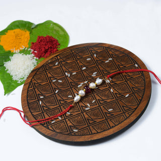 A handcrafted Rubellite Freshwater Pearl Rakhi displayed on a wooden platform with decorative elements in the background.