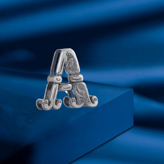 a detailed view of a 925 sterling silver initial 'A' pendant by Nipura, featuring carved designs, resting on a blue surface. 