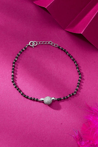 A silver bracelet with black beads and sparkling zircon stones, displayed against a pink background with a feather.